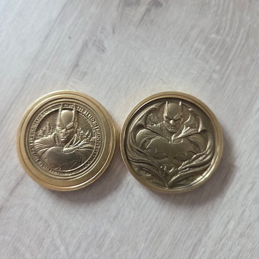 Two gold coins with intricate designs on a light gray surface showing 2 images of batman