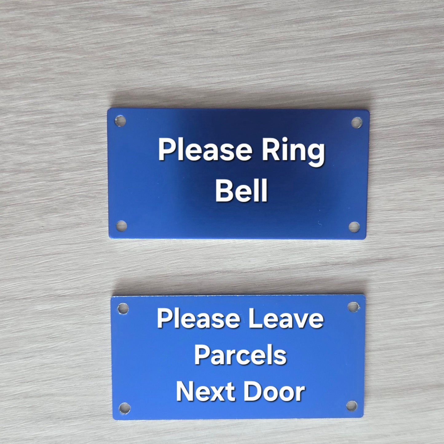 Two blue signs on a textured wall, one instructing to ring the bell and the other to leave parcels next door.