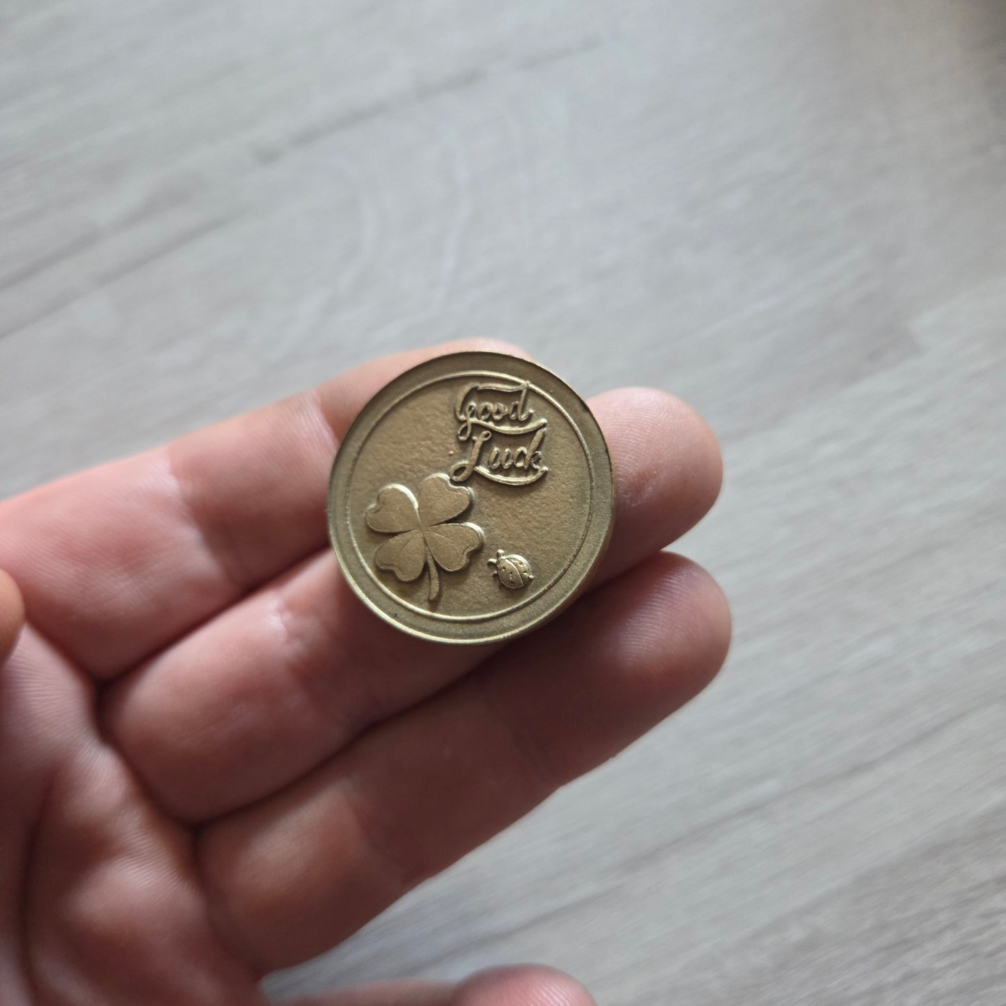 Hand holding a gold coin with a clover design on a light wooden surface