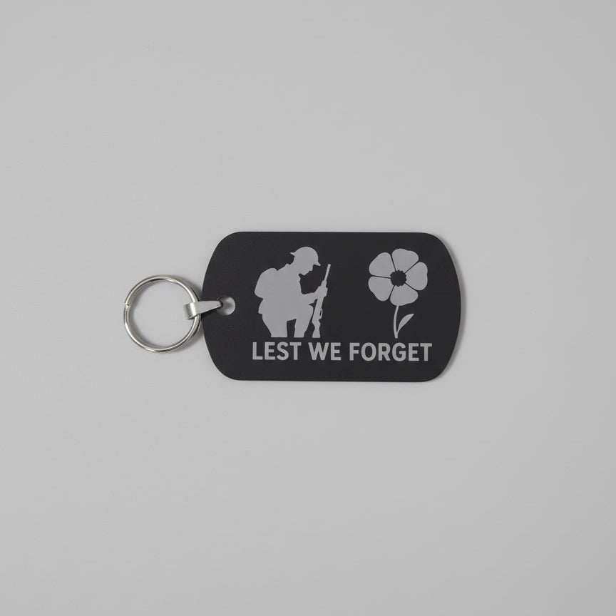 Black keychain with 'Lest We Forget' design on a gray textured background