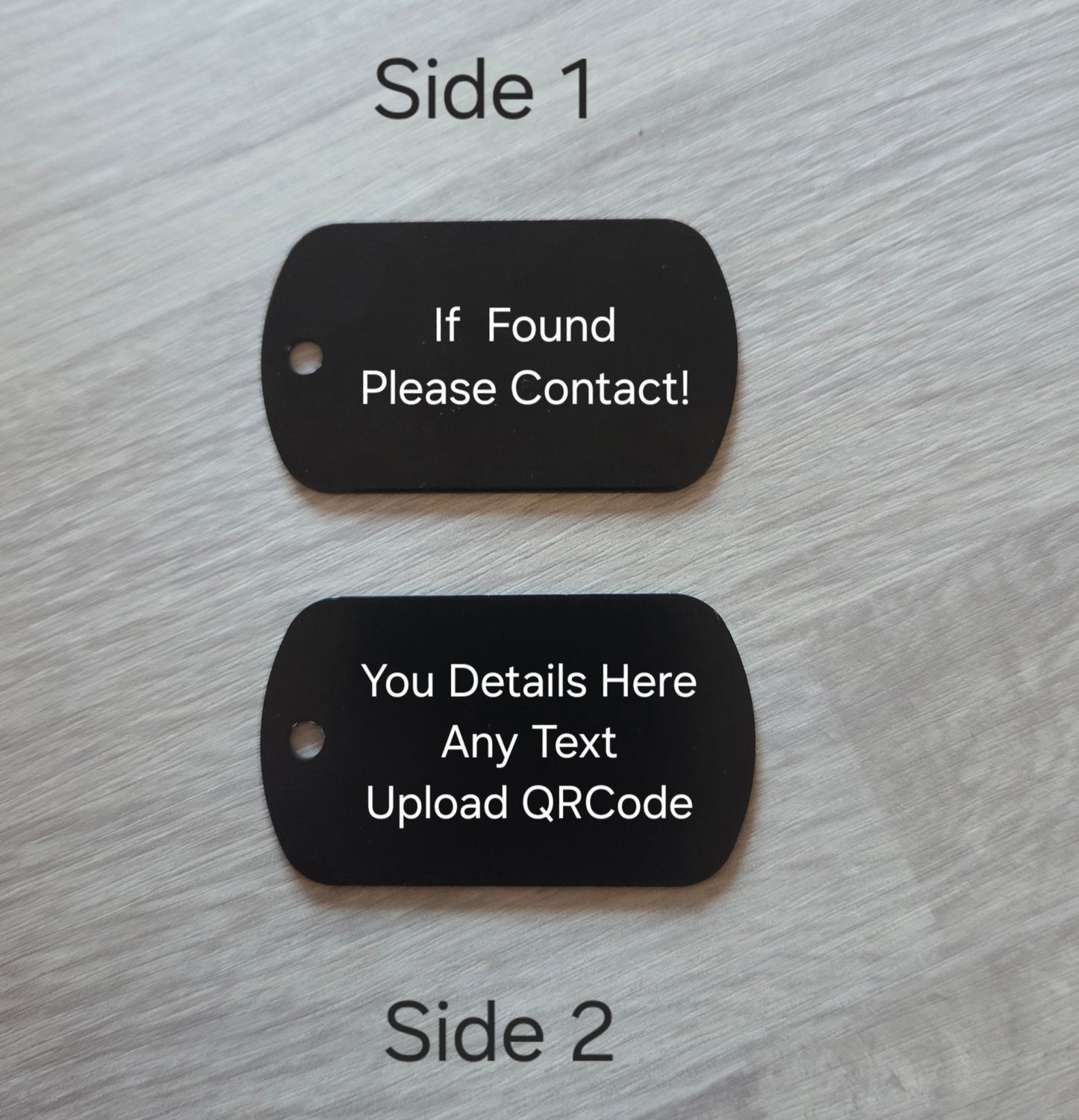 Two black dog tags on a light wood surface with text on each tag.
