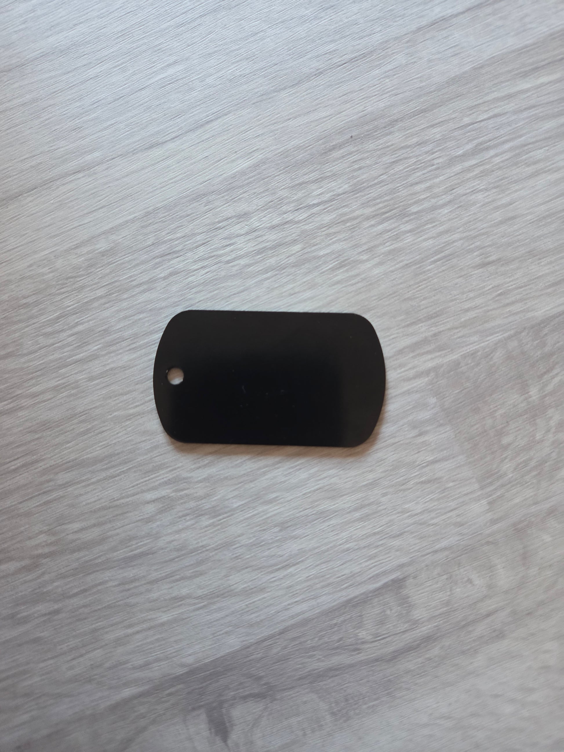 Black rectangular object with a small hole on a gray wooden surface
