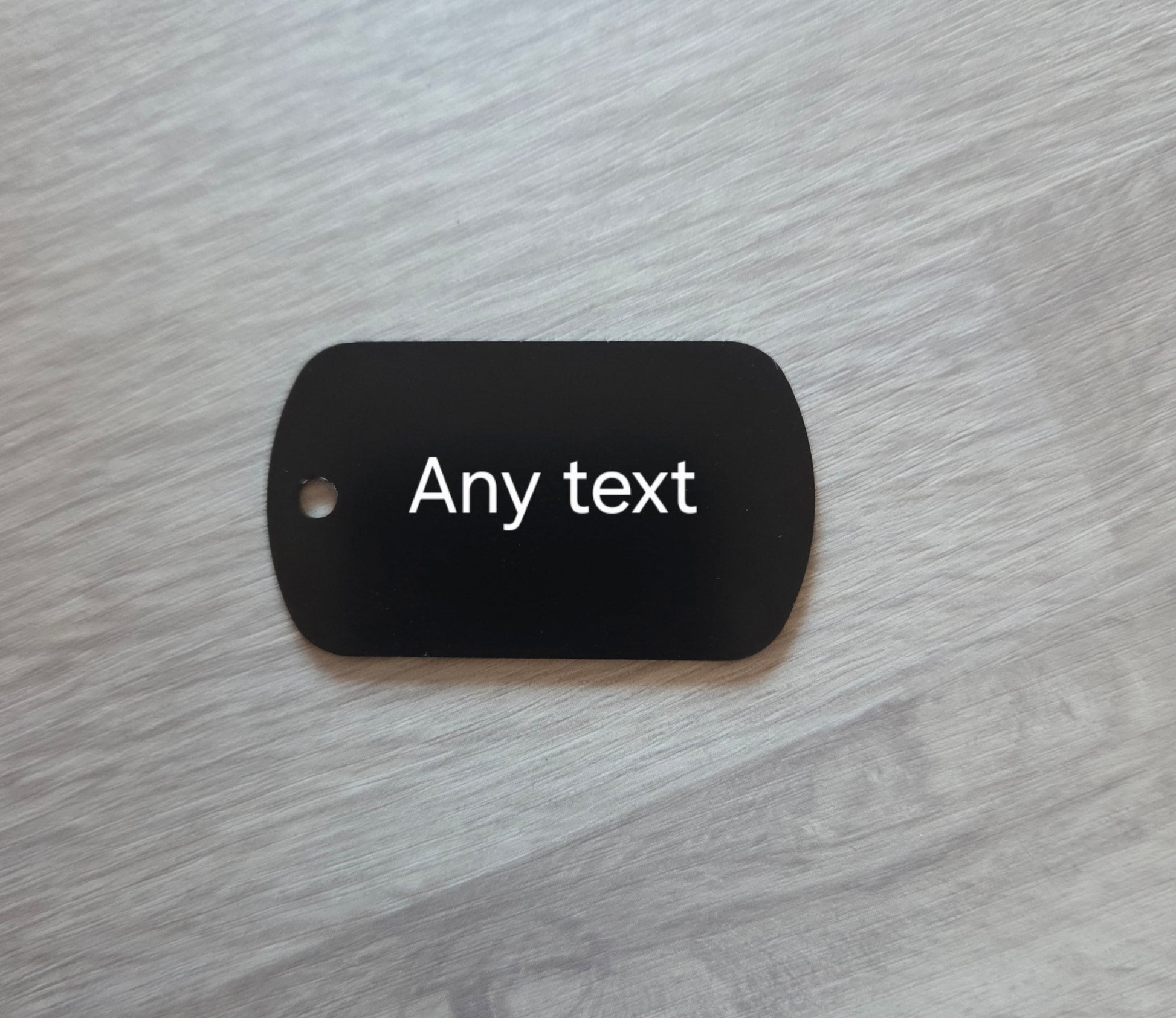 Black dog tag with 'Any text' on a gray surface