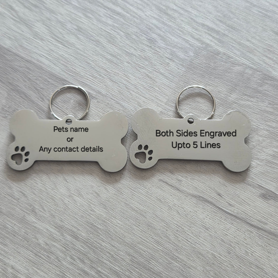 Two bone-shaped pet tags on a gray surface