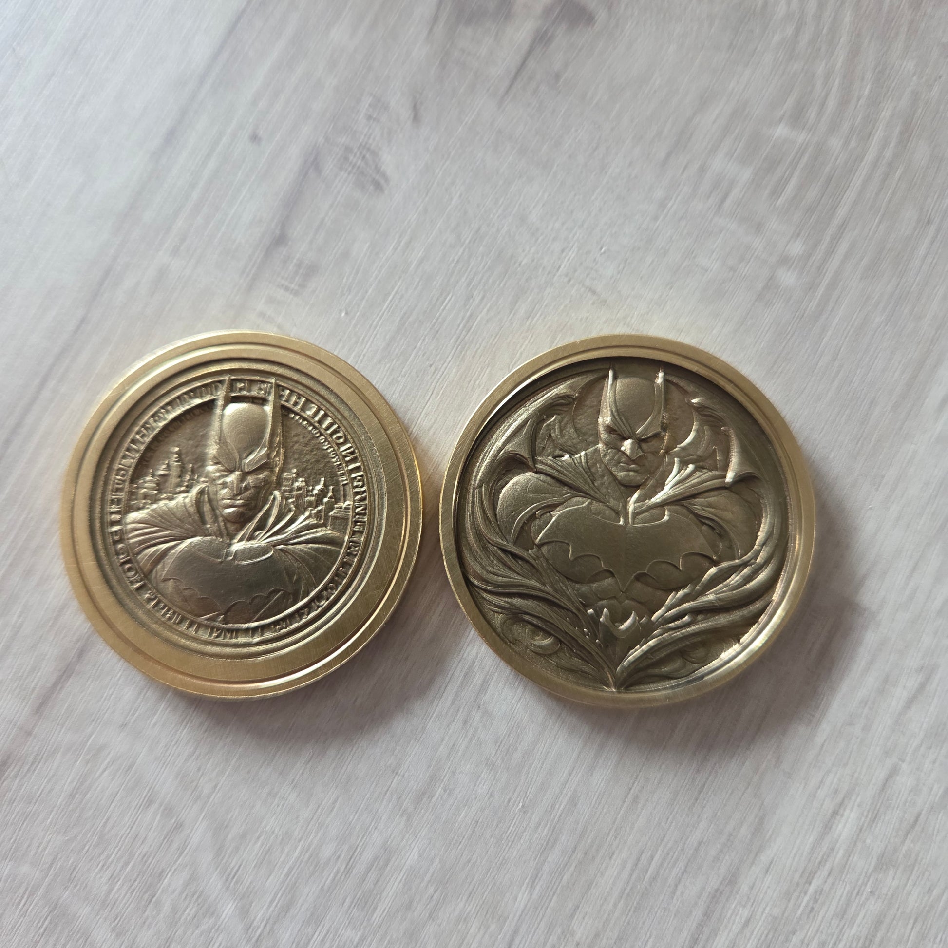 Two gold coins with intricate designs on a light gray surface showing 2 images of batman
