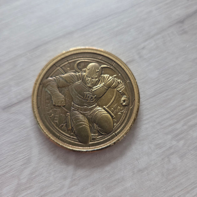 brass coin on a light surface showcasing the embossed image of daredevil 