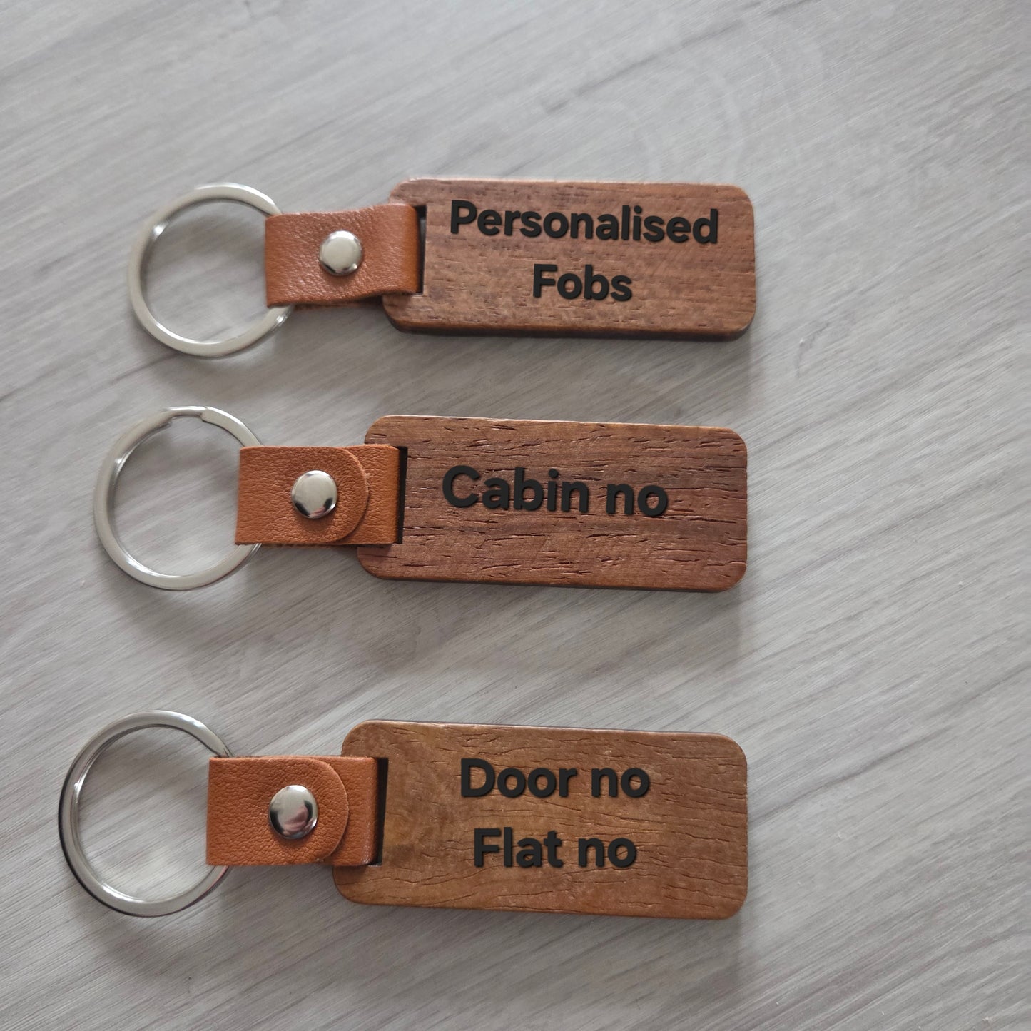 Three wooden keychains with engraved text on a gray surface