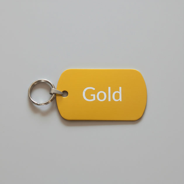 Yellow tag with 'Gold' text and a key ring on a light wooden surface