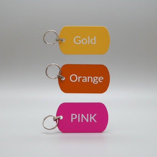Three color-coded keychains labeled 'Gold', 'Orange', and 'Pink' on a light wooden surface.