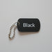 Black dog tag with 'Black' text on a light wooden surface