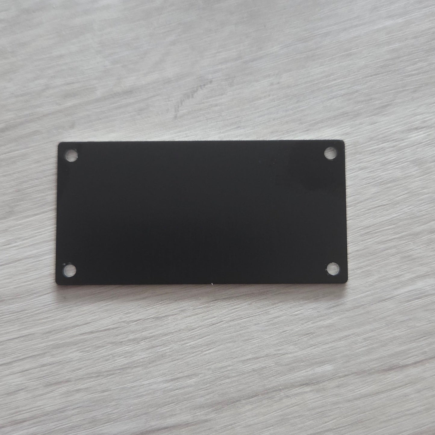 Black rectangular metal plate with two screws on a light gray wooden surface