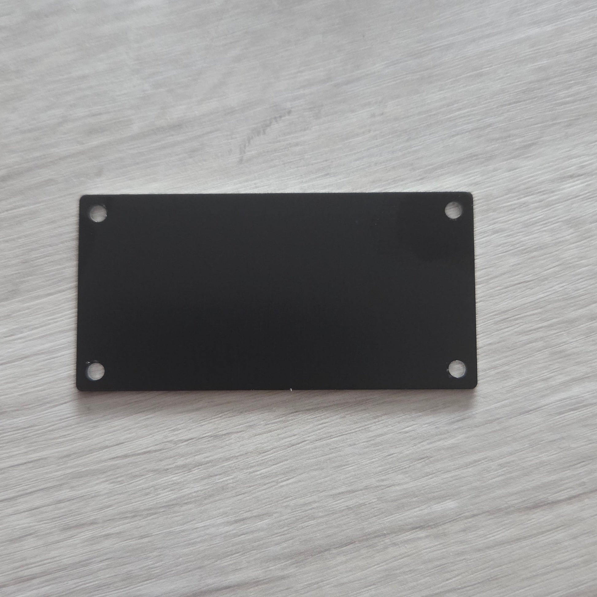 Black rectangular metal plate with two screws on a light gray wooden surface