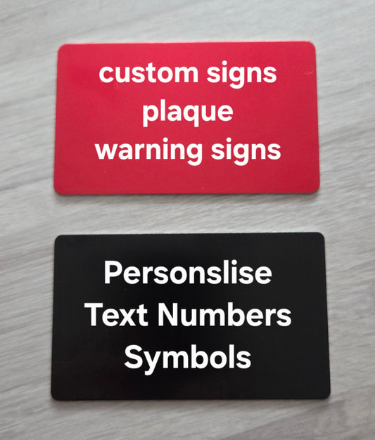 Two customizable signs on a gray surface, one red with white text and one black with white text.