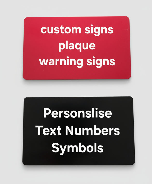 Two customizable signs on a gray surface, one red with white text and one black with white text.