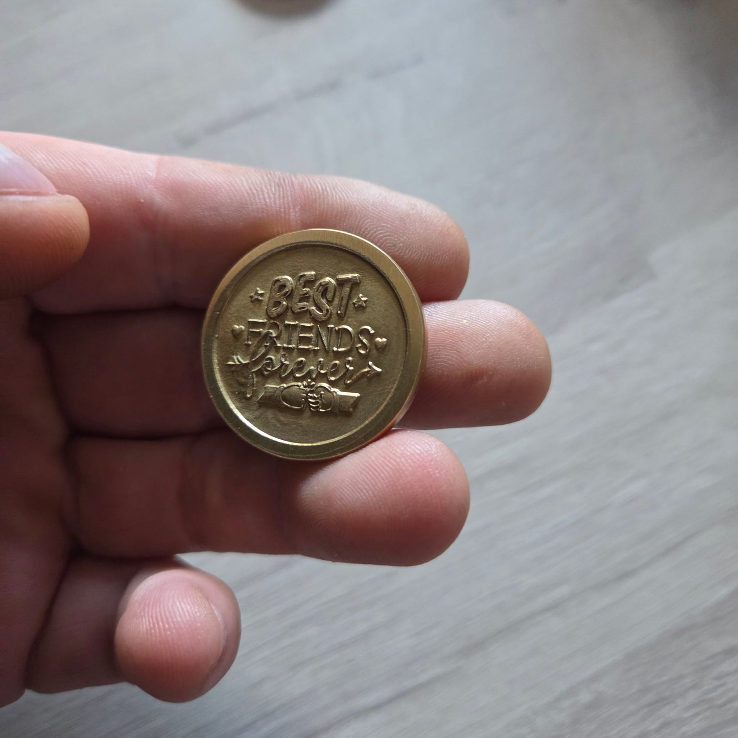 Hand holding a gold coin with intricate designs on a light wooden surface