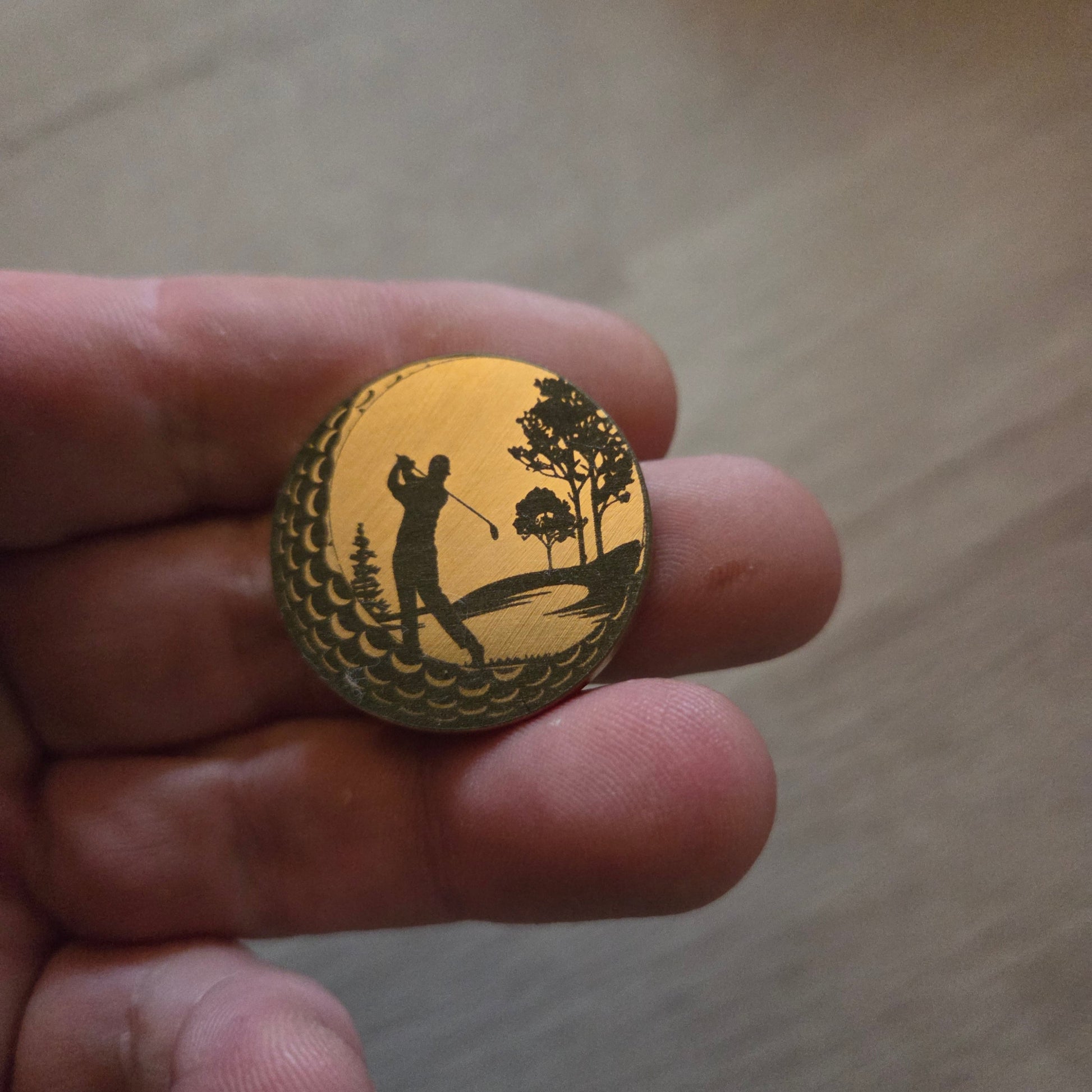 Small round object with a design held between fingers on a light wooden surface