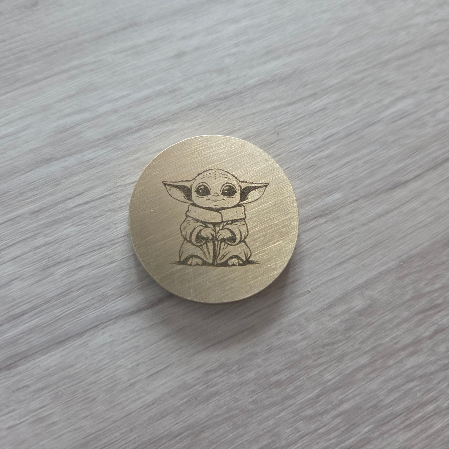 Round wooden button with a Yoda design on a gray surface