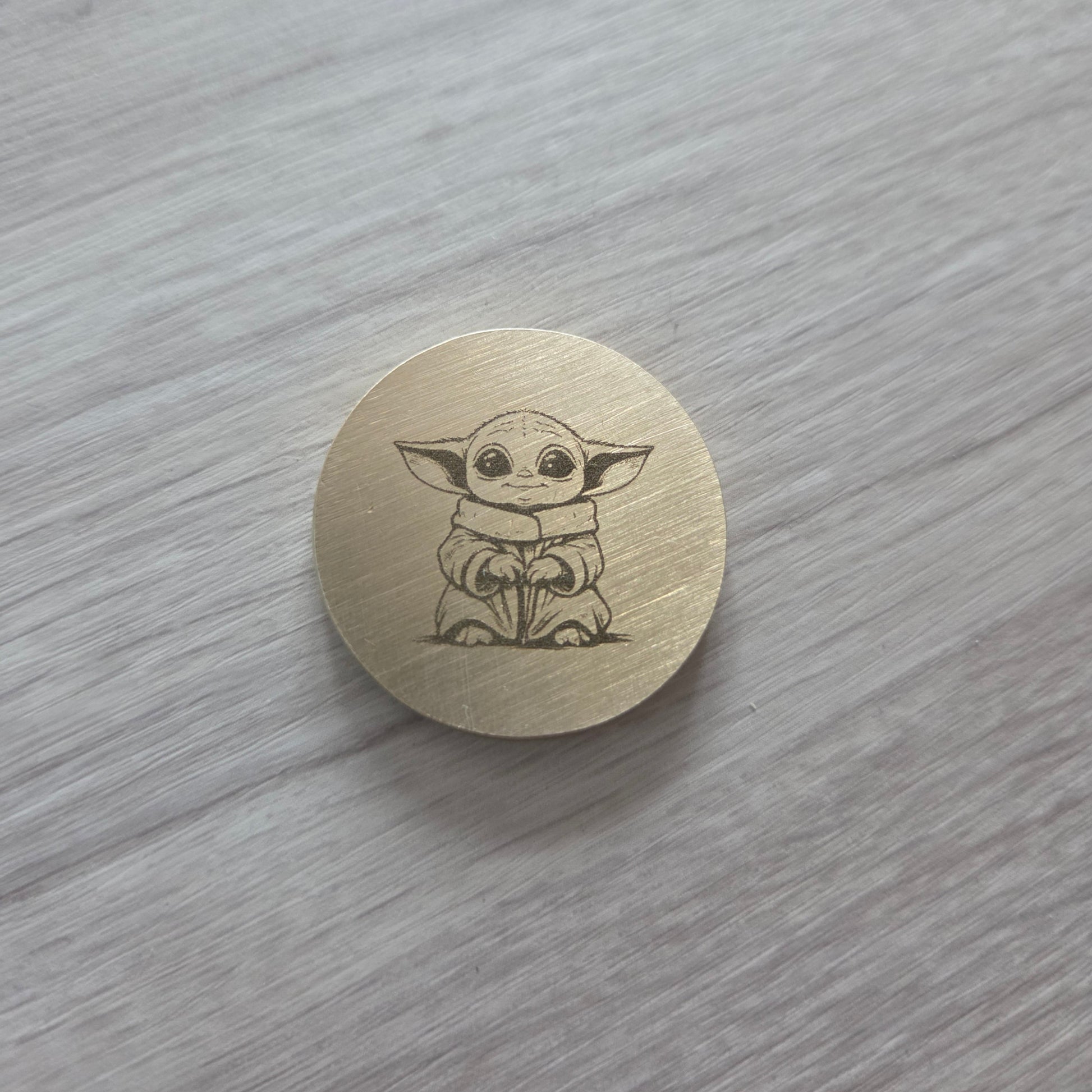 Round wooden button with a Yoda design on a gray surface